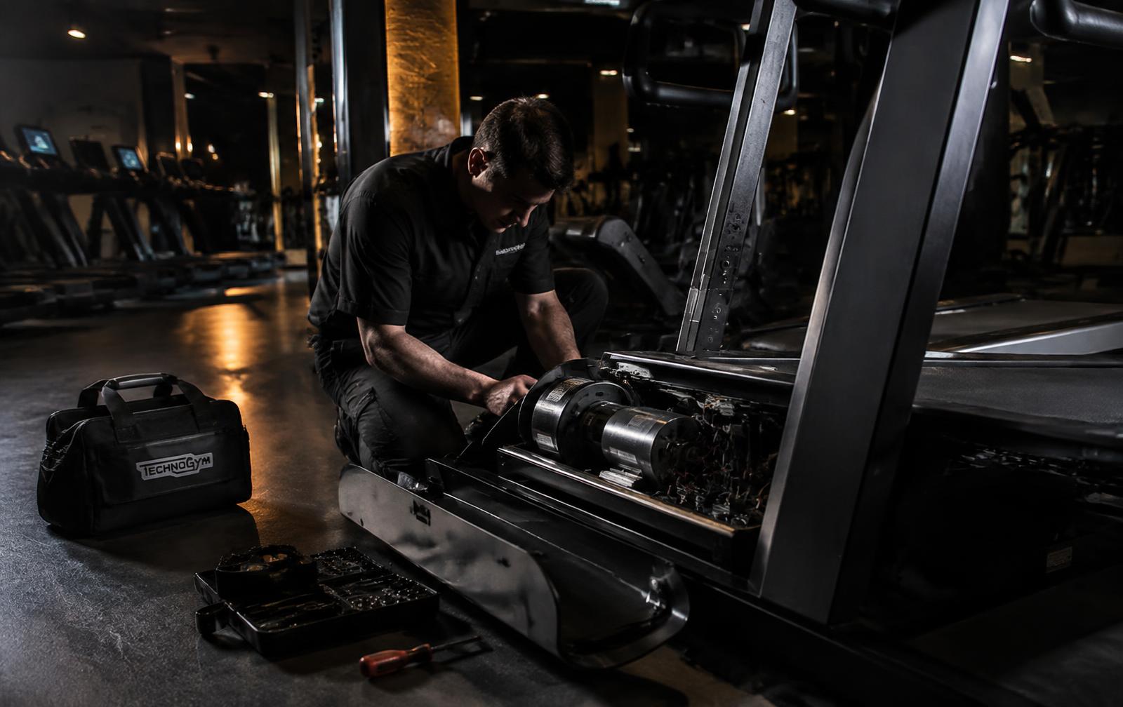 Technician servicing the motor of a commercial treadmill in a gym